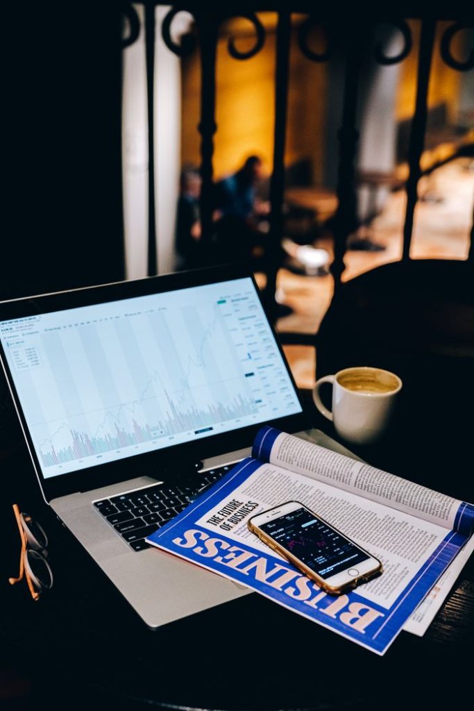 The Art of Drawing Readers In: Your attractive post title goes here A laptop showing financial charts beside a business magazine and coffee cup in a cafe setting.